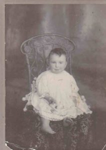 Historic photo of a young child in white gown sitting on decorative carved chair