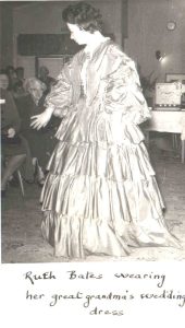 Black and white photo of Ruth Bates modeling her great grandmothers wedding dress from 1859, a long sleeve floor length gown with lots of layers in 1963