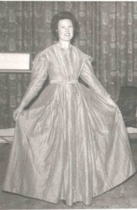 Black and white photo of Woman modeling long sleeve, floor length gown