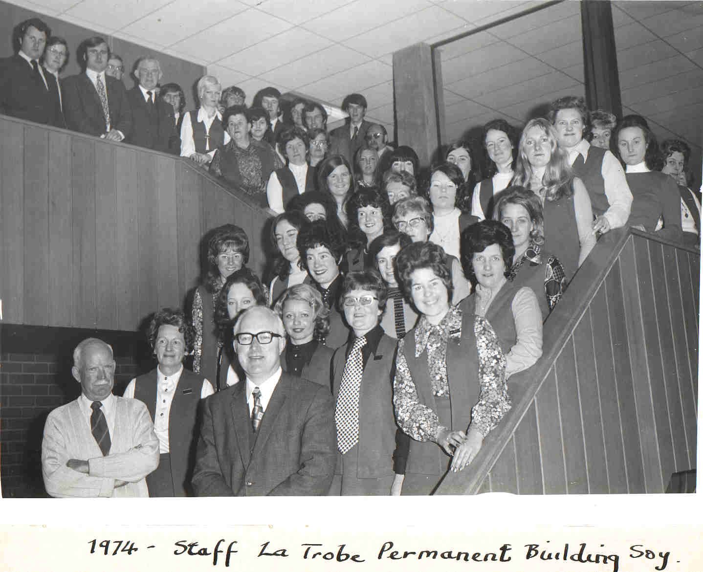 Black and white photo from 1974 of lots of men and women standing in office staircase