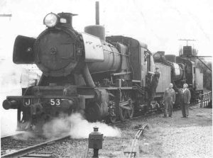 Historic photo of stopped steam train with driver and two men next to it.