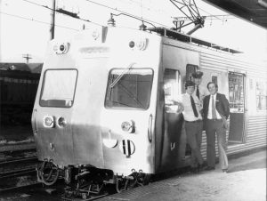 Black and whit ephoto of silver metro train with three men standing next to it, 1977