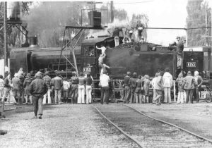 Black and white photo of a crowd of people gathered around a steam train while it refuels in Traralgon, 1978