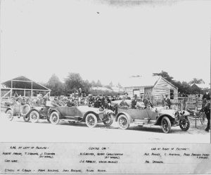 Historic photo fo three open top cars in a row with people in them, and a crowd around them