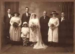 Historic photo of a wedding party in 1921 with bride and groom, Father of the bride, two matrons of honour, two groomsmen and one flower girl.