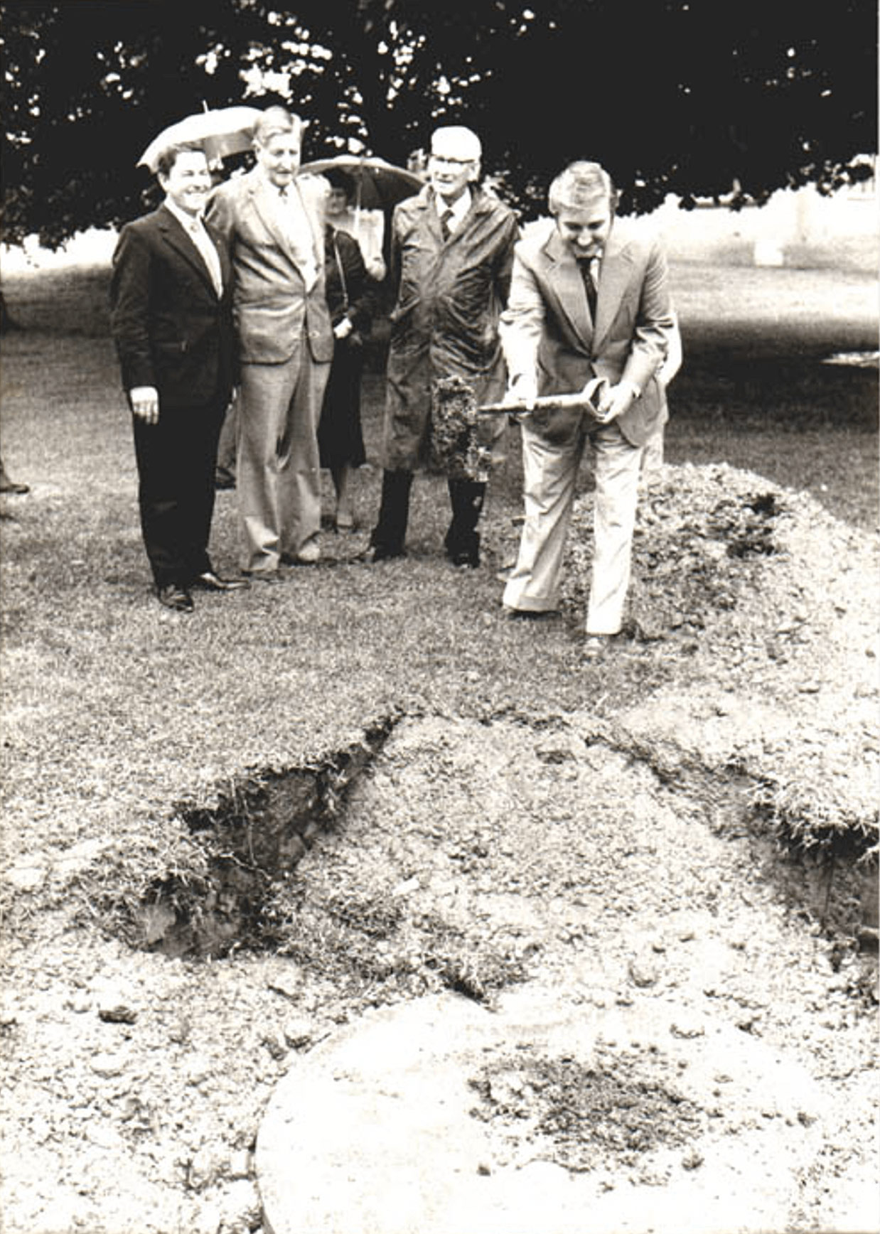 Black and white photo of four men helping to cover a time capsule in a park